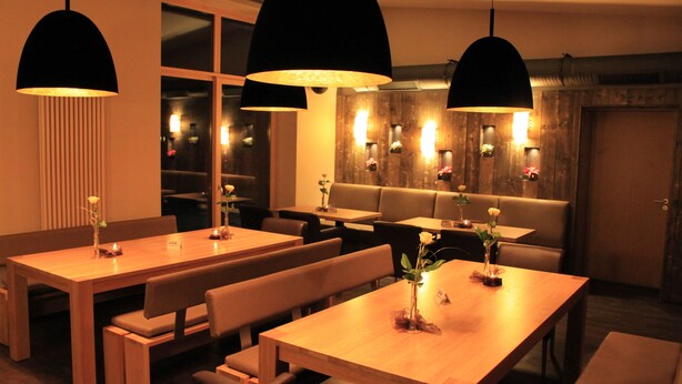 A restaurant with wooden tables and benches, pendant lighting, and a cozy ambiance. - Troll's Brauhaus Hotel (Medebach)