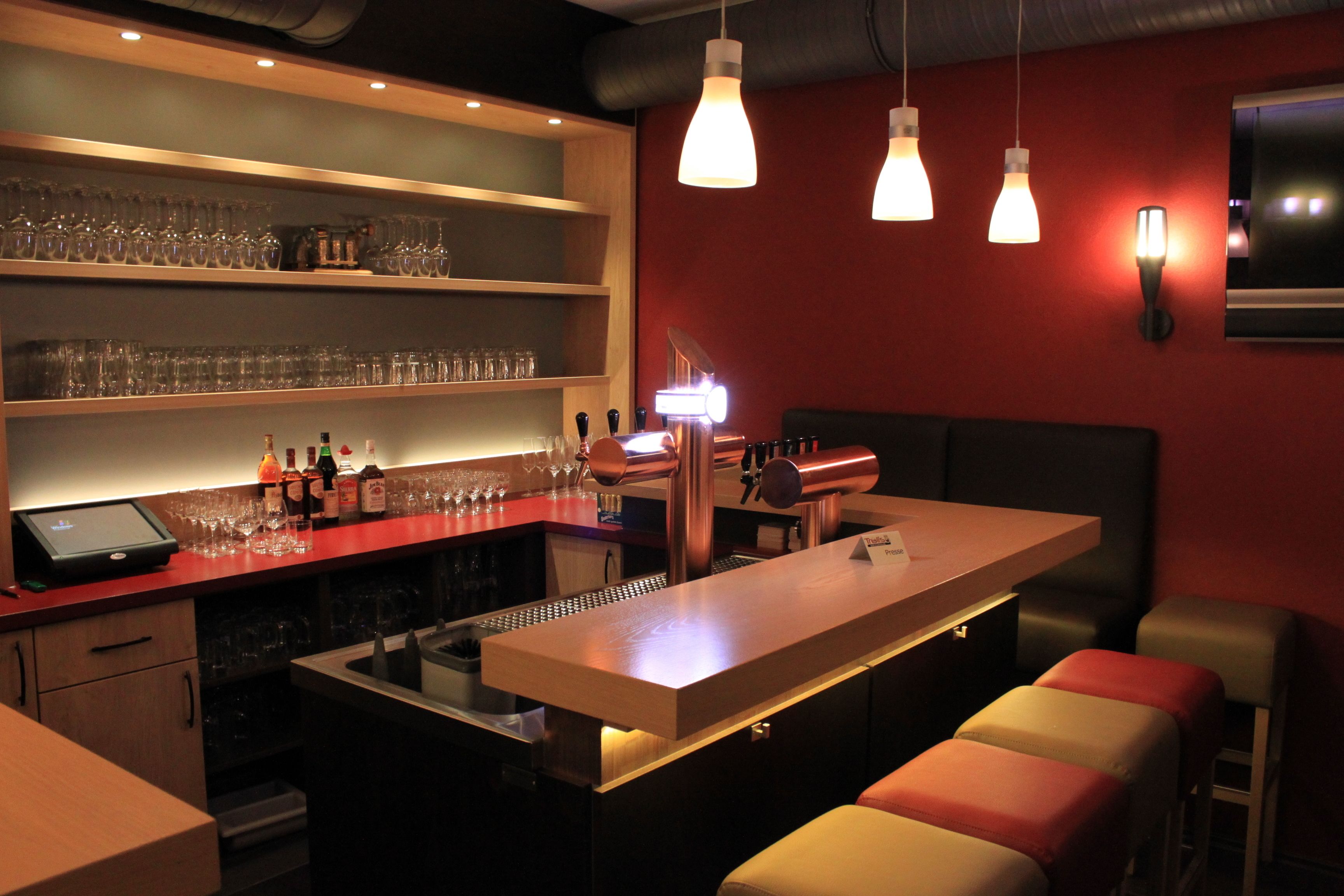 A bar area with a counter, stools, and shelves with glasses and bottles.