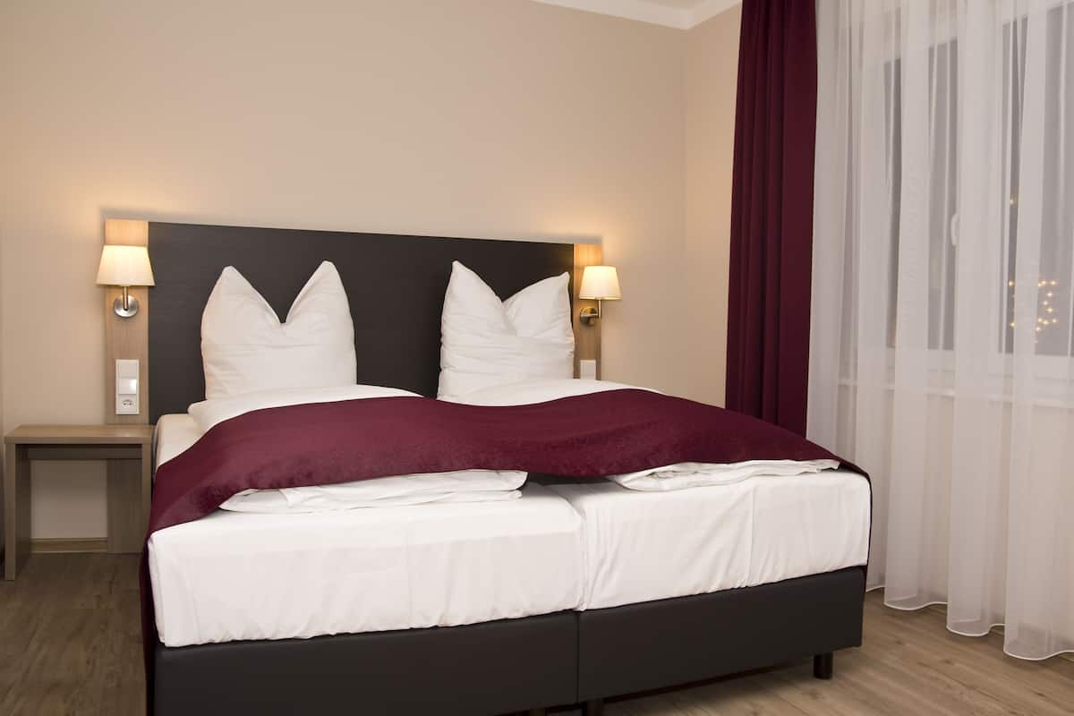 A neatly made bed with white linens and a dark headboard, two bedside lamps, and a wooden nightstand.
