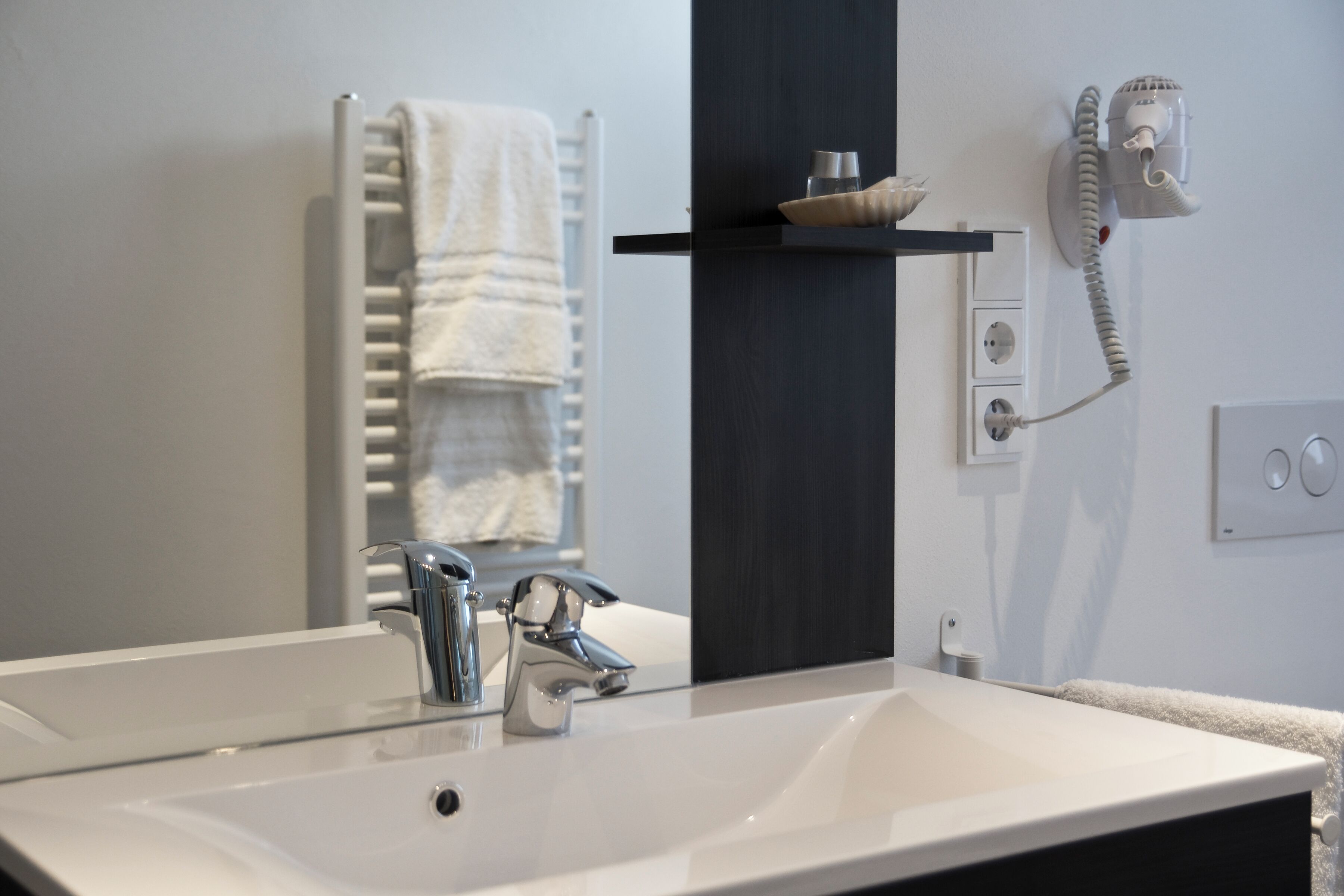 A bathroom with a white sink, chrome faucet, and a towel rack. There is a towel hanging on the rack.