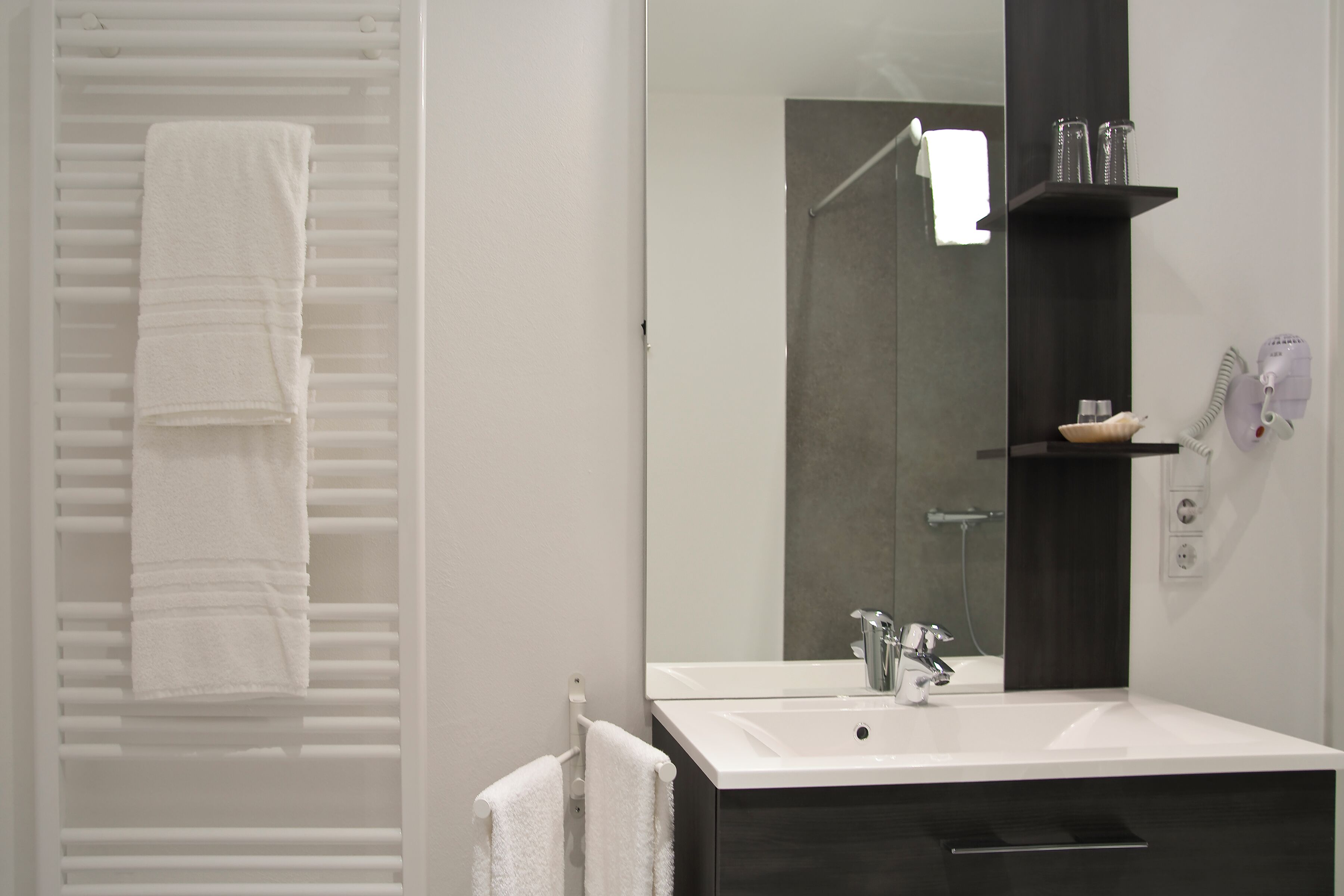 A modern bathroom with a white sink, a large mirror, and a towel rack with folded towels.