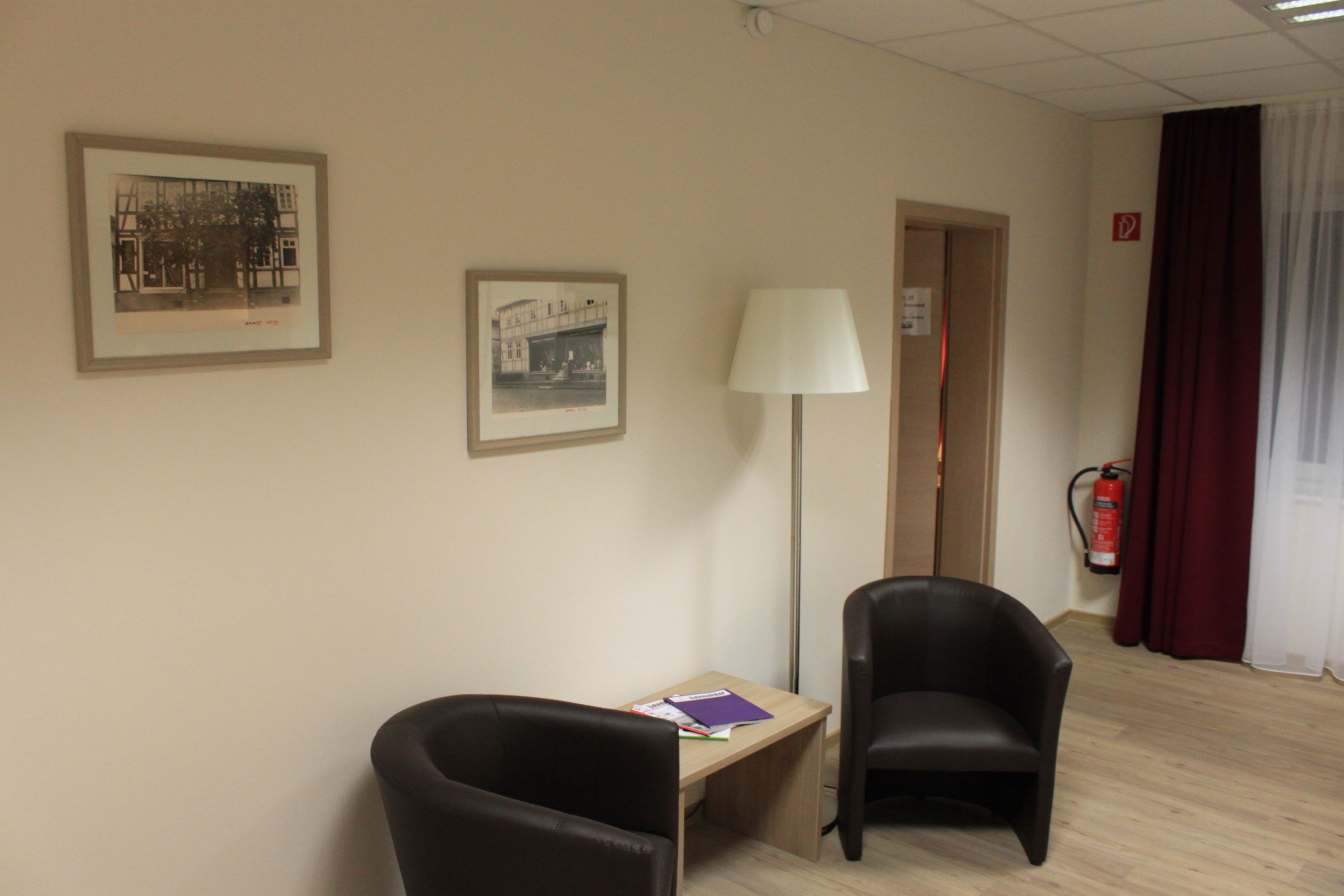 A hotel room with two chairs, a desk, a lamp, and framed pictures on the wall.