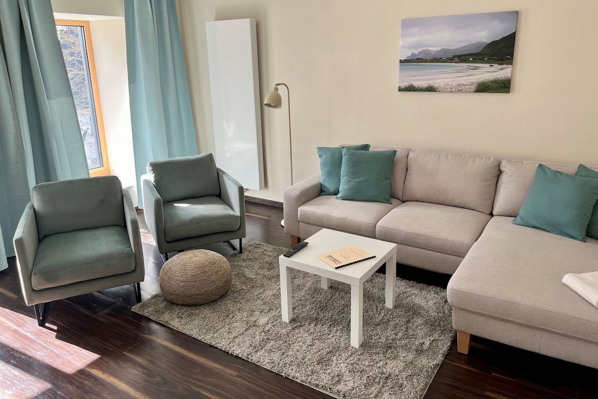 A modern living room with a sofa, two armchairs, a coffee table, and a painting on the wall.