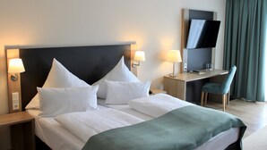 A hotel room with a large bed, two bedside tables with lamps, a desk with a chair, a flat-screen TV, and a window with curtains. - Troll's Brauhaus Hotel (Medebach)