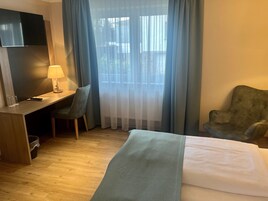 A hotel room with a bed, a desk with a lamp, two chairs, and a TV.