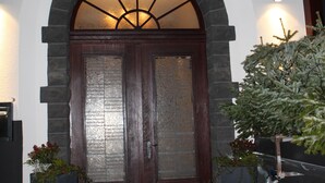 A building entrance with a sign reading "Brauhaus" above a double door with a stone archway. There are two large planters with plants on either side of the entrance. - Troll's Brauhaus Hotel (Medebach)