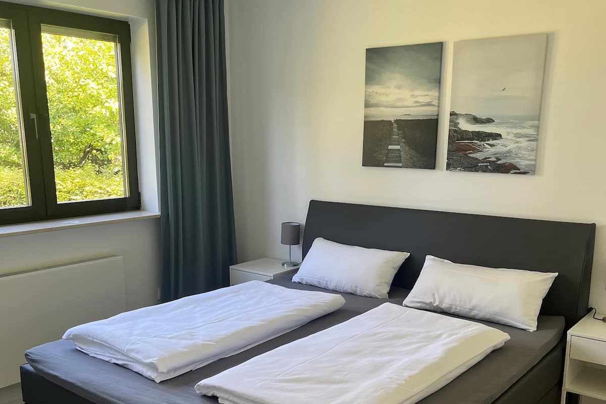 A modern bedroom with a large bed, a nightstand, a lamp, and two framed pictures on the wall.