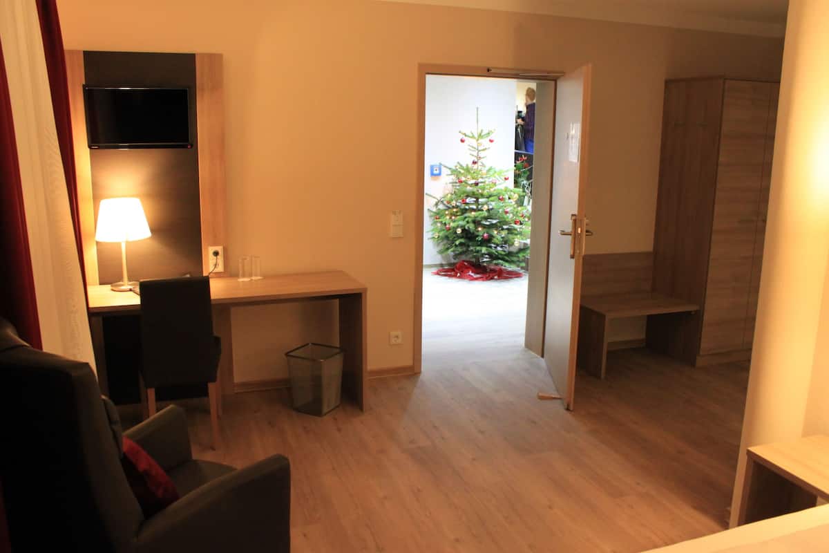 A room with a desk, chair, and a television mounted on the wall. There is a Christmas tree in the background.