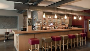 A bar area with wooden stools, a bar counter, and hanging pendant lights. - Troll's Brauhaus Hotel (Medebach)