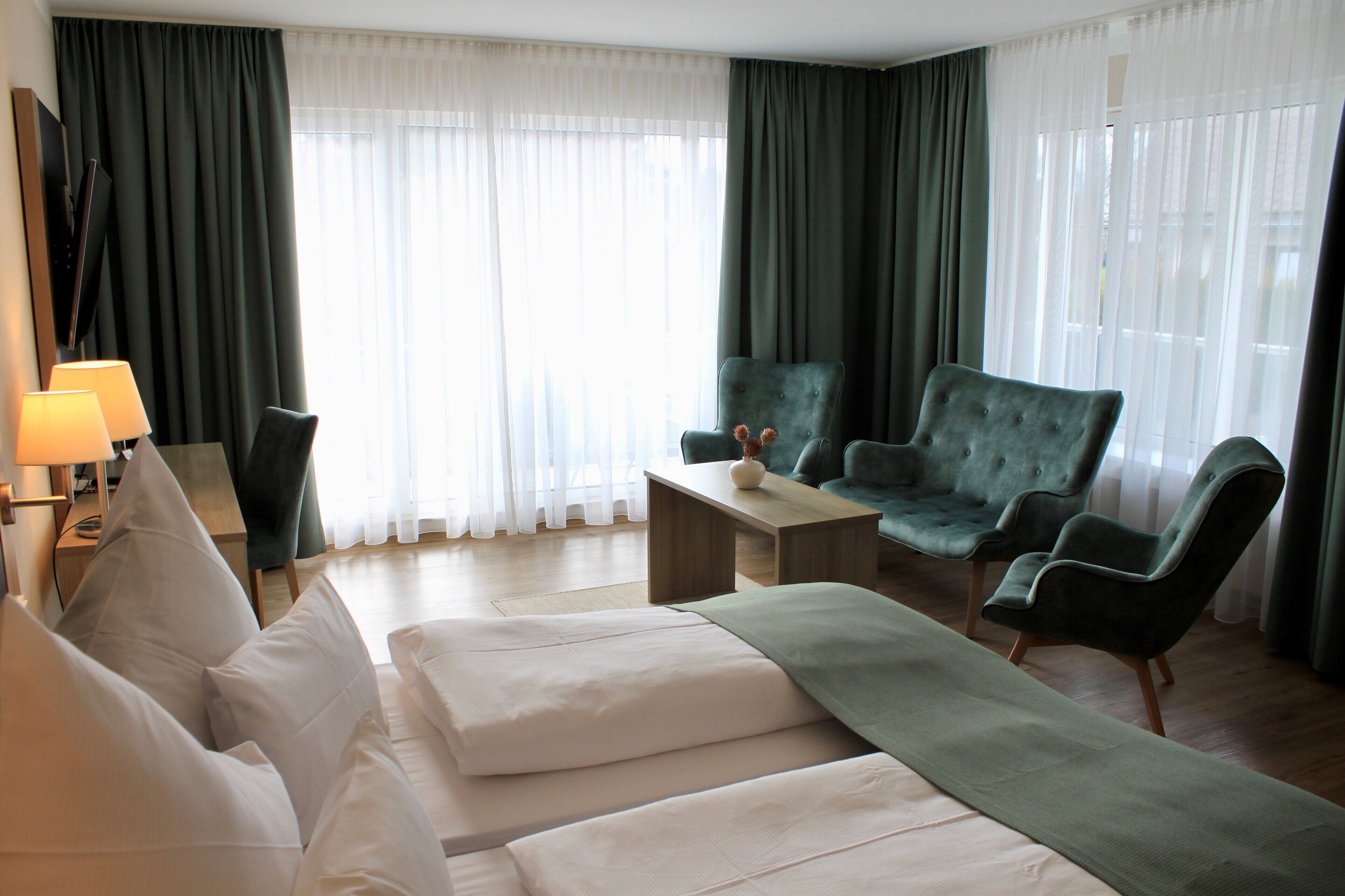 A modern hotel room with a large bed, a green armchair, a wooden coffee table, and a TV on a stand.