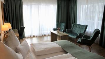 A modern hotel room with a large bed, a green armchair, a wooden coffee table, and a TV on a stand.