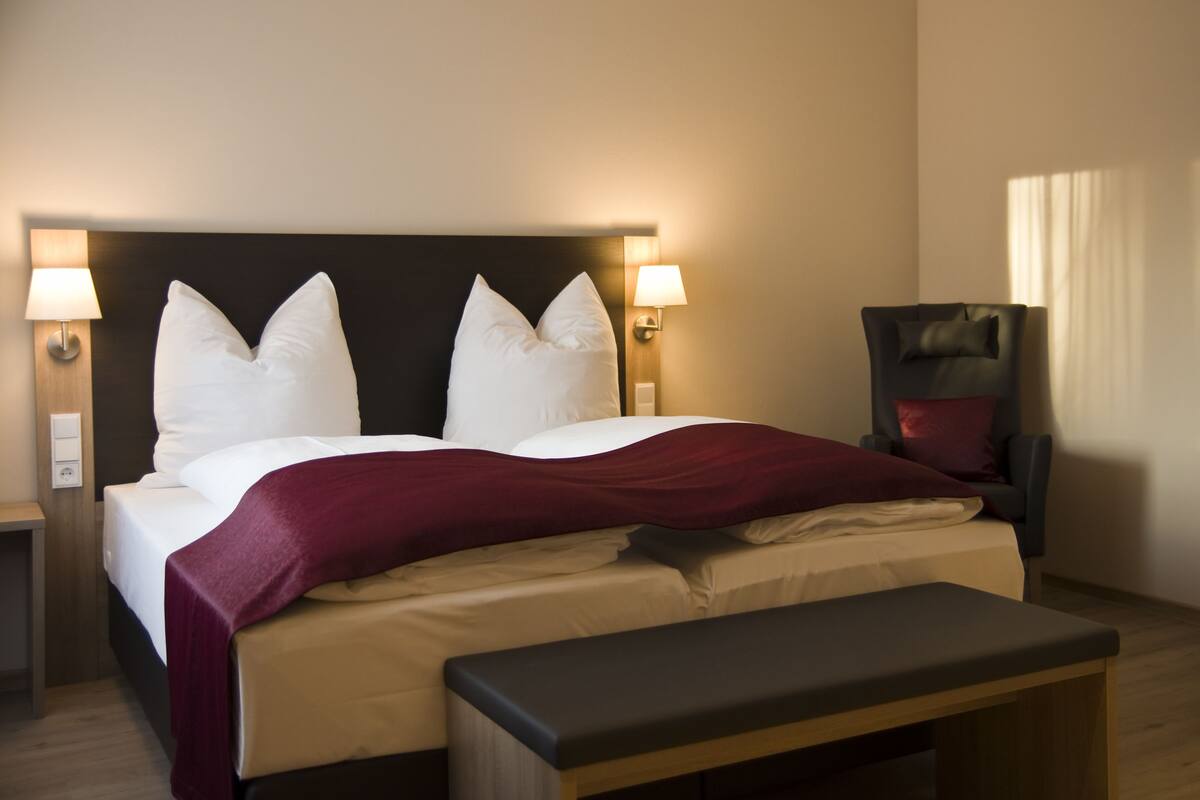 A hotel room with a large bed, two bedside lamps, a chair, and a bench.
