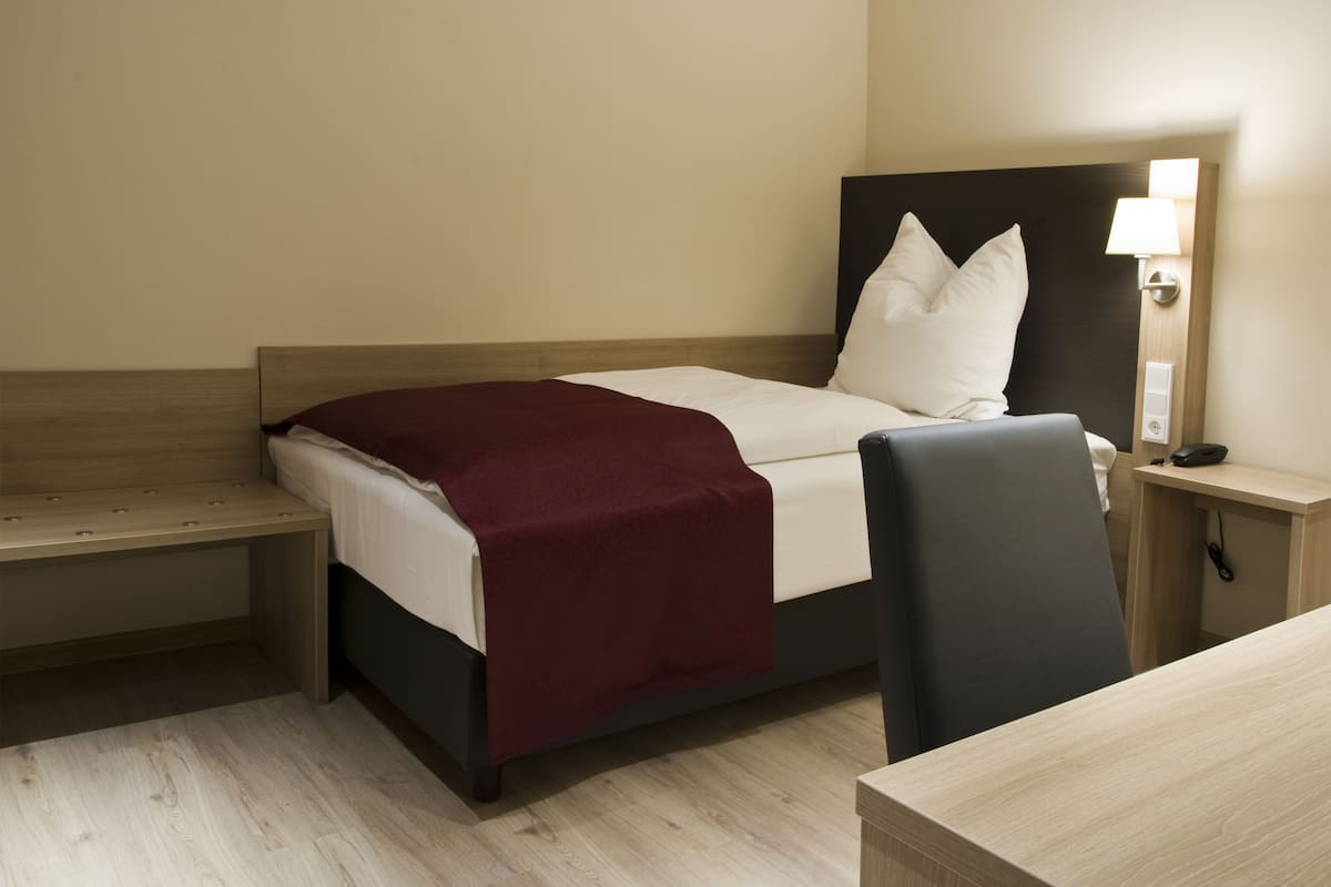 A hotel room with a bed, a desk, a chair, a nightstand, and a lamp.