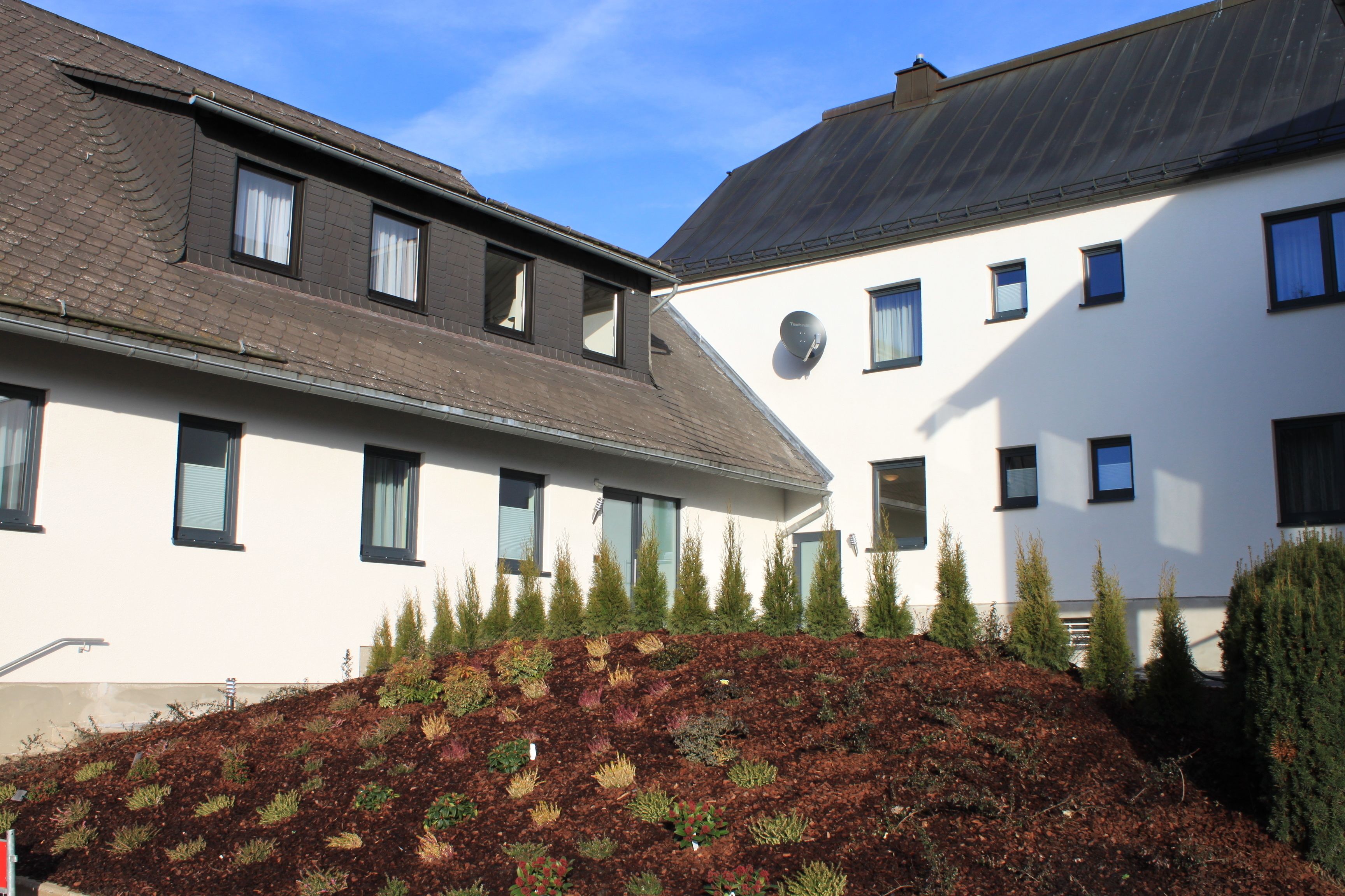A building with a sloped roof, multiple windows, and a landscaped area with various plants.