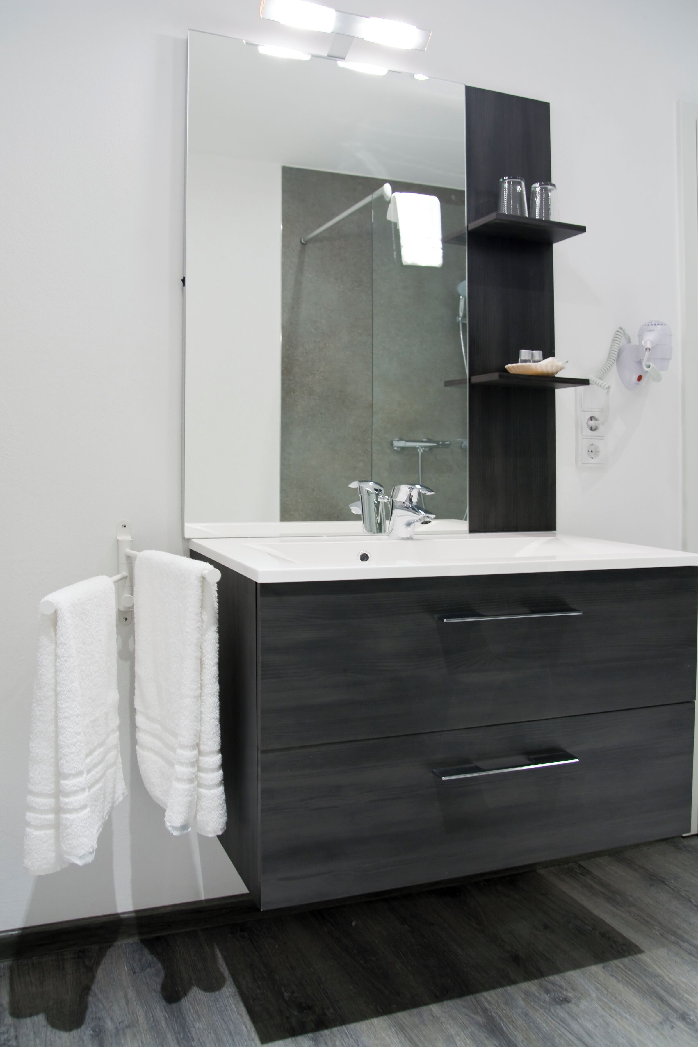 Une salle de bain moderne avec un grand miroir, des meubles de couleur sombre et un plan de travail blanc.