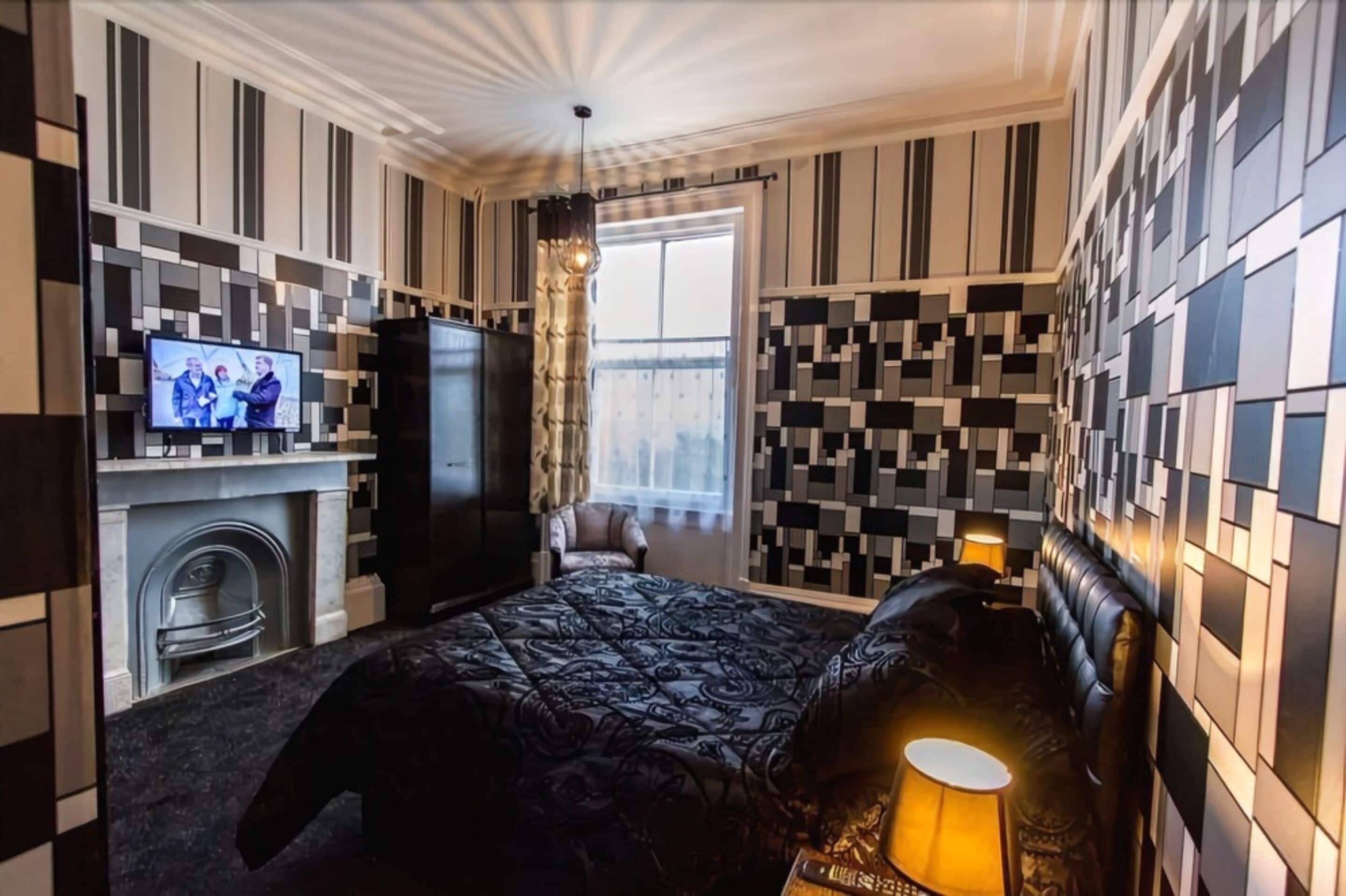 A modern hotel room with a large bed, a television, a fireplace, and a view of the outdoors.