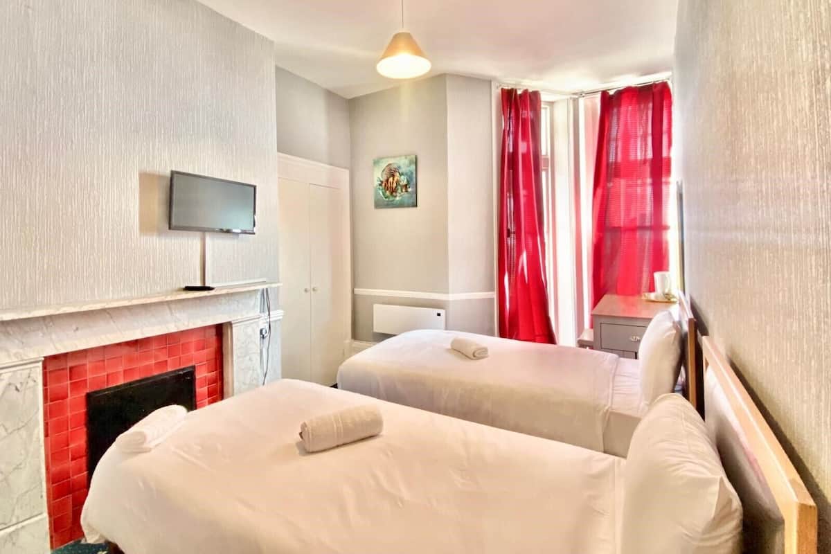 A hotel room with two beds, a TV mounted on the wall, a fireplace, and red curtains.