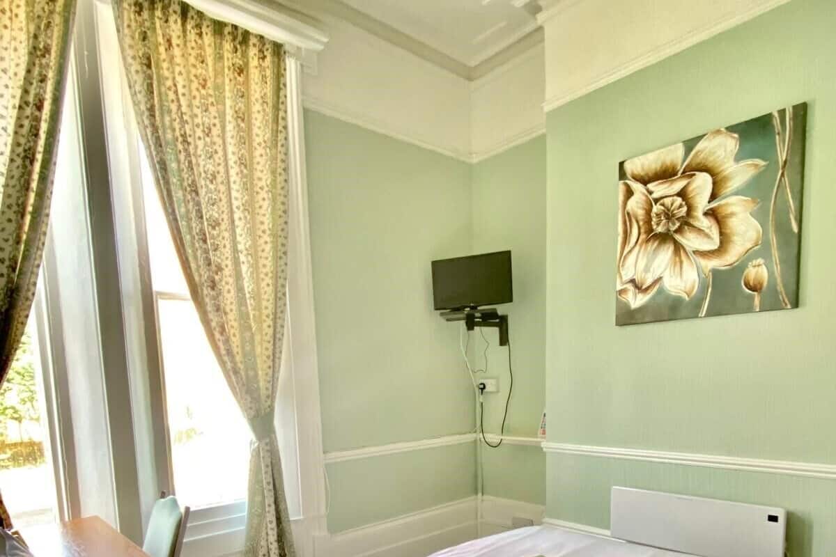 A hotel room with a bed, a desk, and a television mounted on the wall.