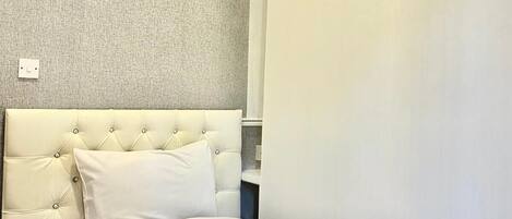 Une chambre d’hôtel avec une tête de lit capitonnée, un lit bien fait avec du linge de lit blanc et une serviette roulée posée sur le lit.