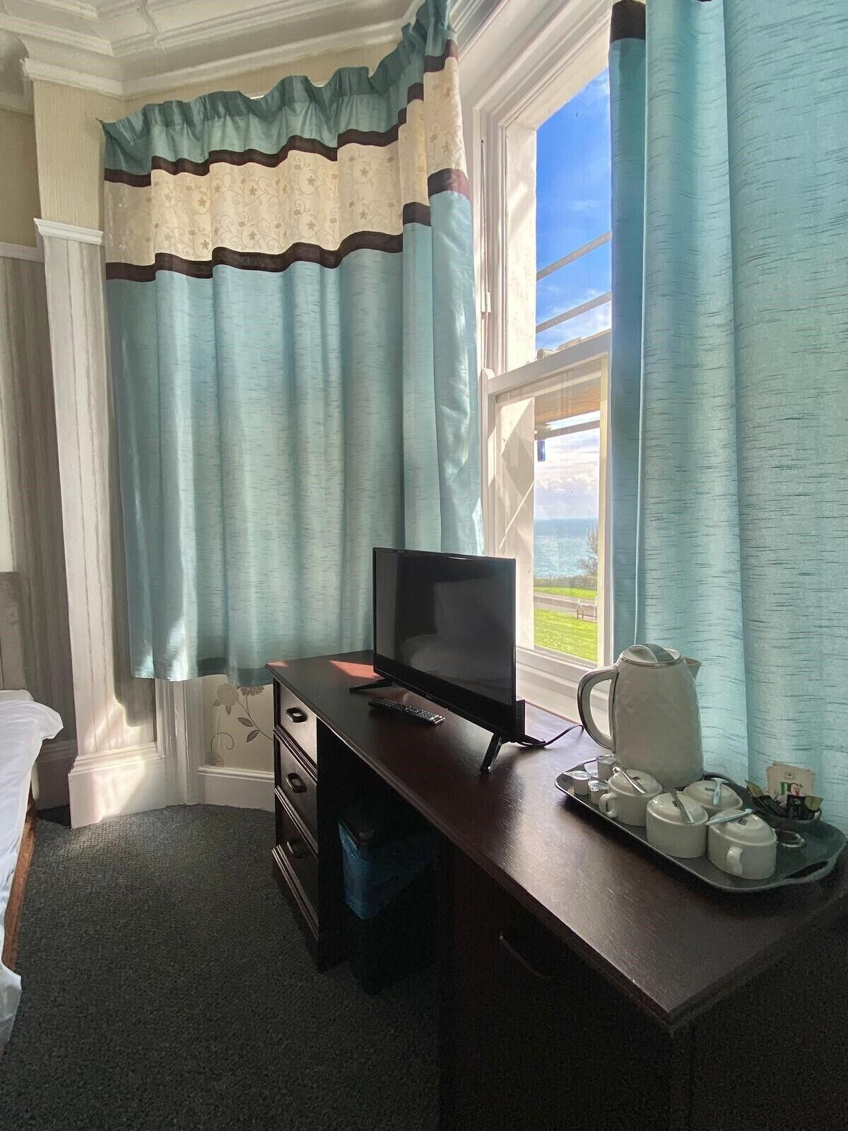A room with a desk, a computer, a coffee maker, and a tray with cups and a pitcher.