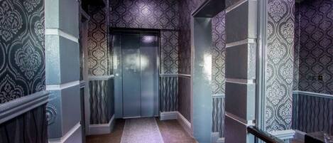 A hallway with patterned wallpaper, a carpeted floor, and a glass elevator.