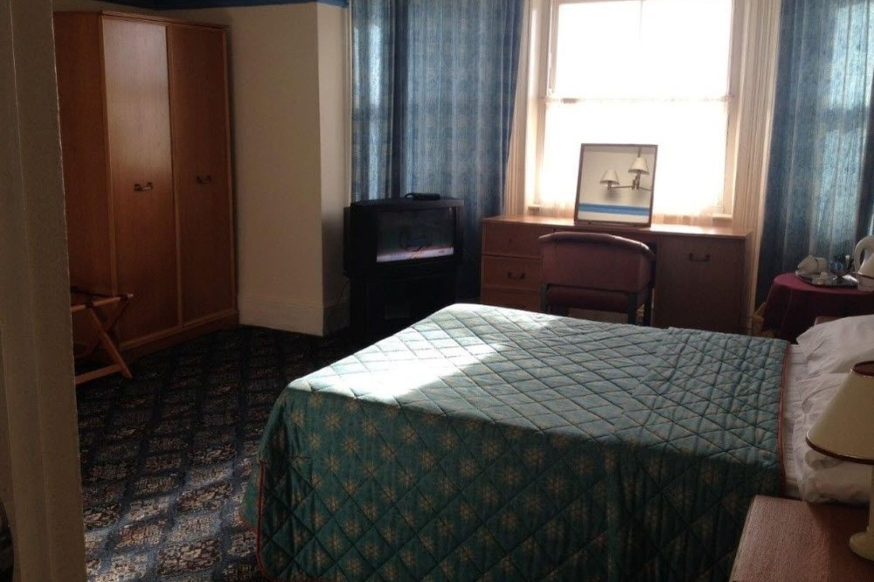 A bedroom with a bed, a desk, a chair, a wardrobe, and a television.