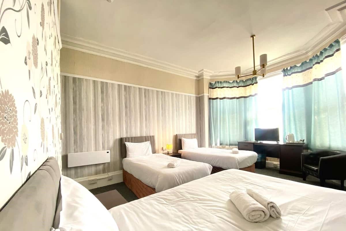 A hotel room with two single beds, a desk with a chair, a television, and a window with curtains.