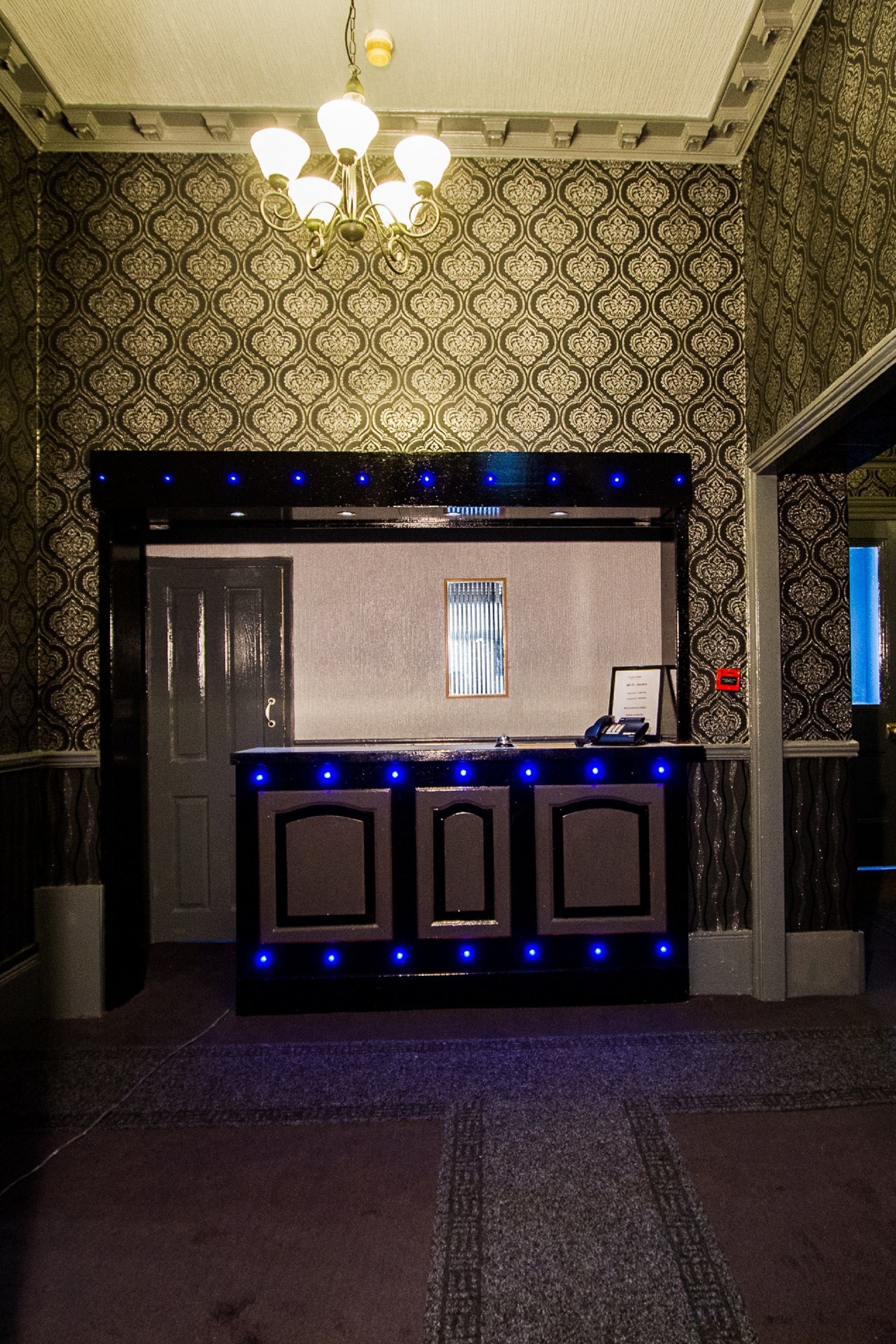 A reception desk with a patterned wallpaper background, a chandelier, and a framed sign above the desk.