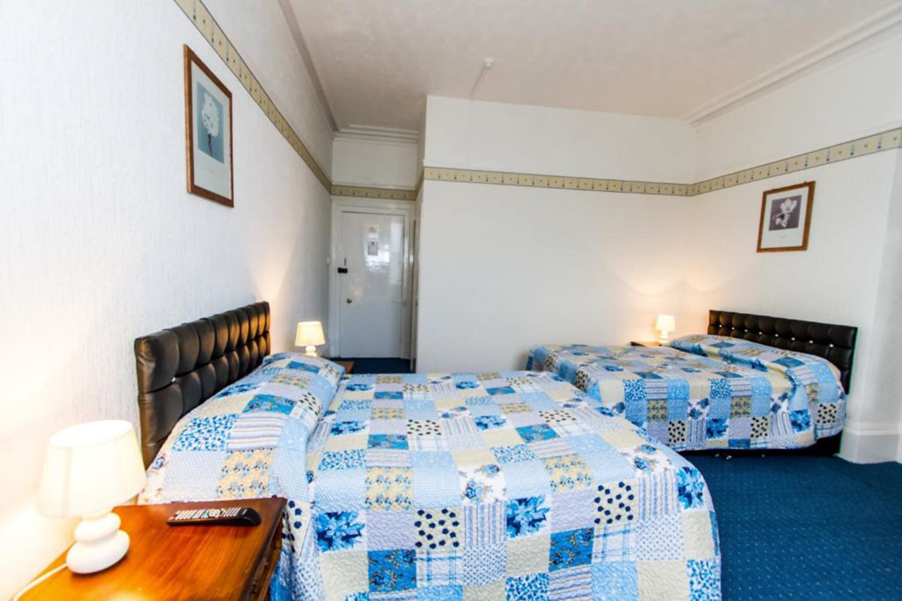 A hotel room with two beds, a wooden nightstand, a lamp, and a door.