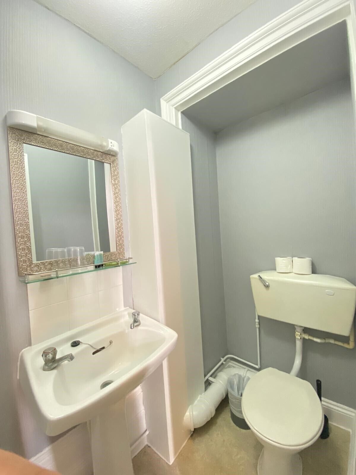 Un baño con lavamanos blanco, repisa de vidrio con artículos de tocador, inodoro y zona de ducha.