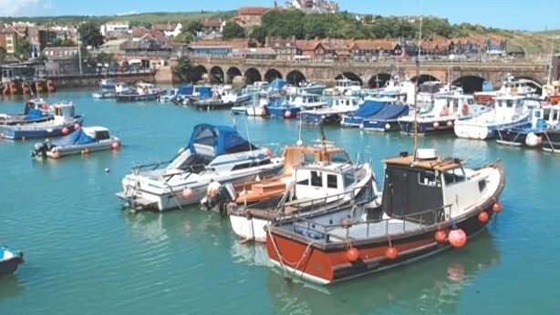 A marina with various boats docked, a bridge in the background, and buildings on a hill. - The Carlton Hotel (Folkestone)