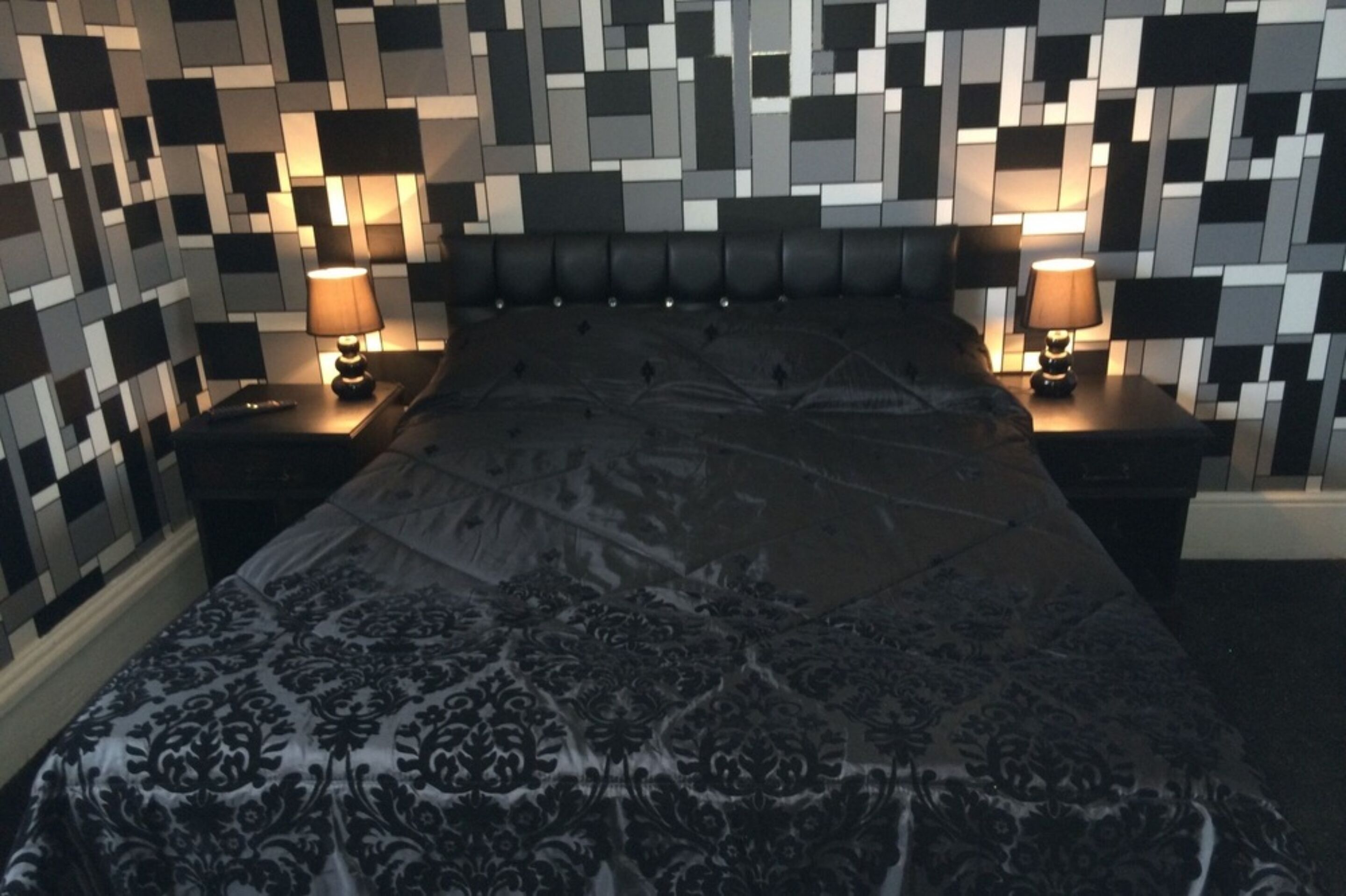Une chambre avec un grand lit, deux tables de chevet et un mur orné d’un motif pixélisé.