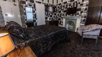 A bedroom with a bed, a chair, a desk, a television, and a fireplace.