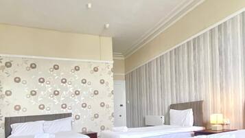 Una habitación de hotel con tres camas, un candelabro, papel tapiz con motivos florales y una cortina a rayas.