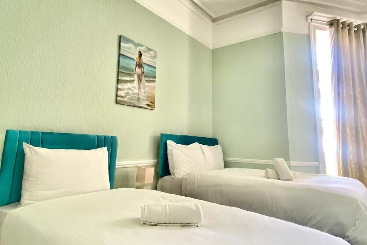 A hotel room with two beds, light green walls, and a painting of a woman on the wall.