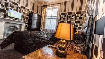 A hotel room with a bed, a wooden nightstand with a lamp, a television, and a fireplace.
