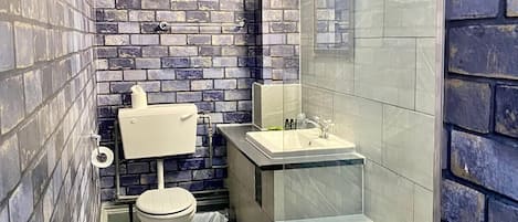 A bathroom with a toilet, sink, and bathtub, featuring blue brick walls and a herringbone floor pattern.