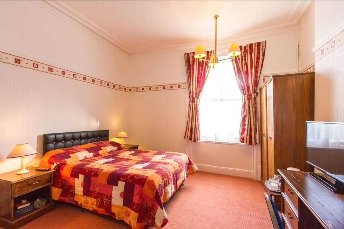 A hotel room with a large bed, a television, a nightstand, and a window with curtains.