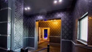 A hallway with patterned wallpaper and a carpeted floor, leading to a room with a blue-lit door. - The Carlton Hotel (Folkestone)