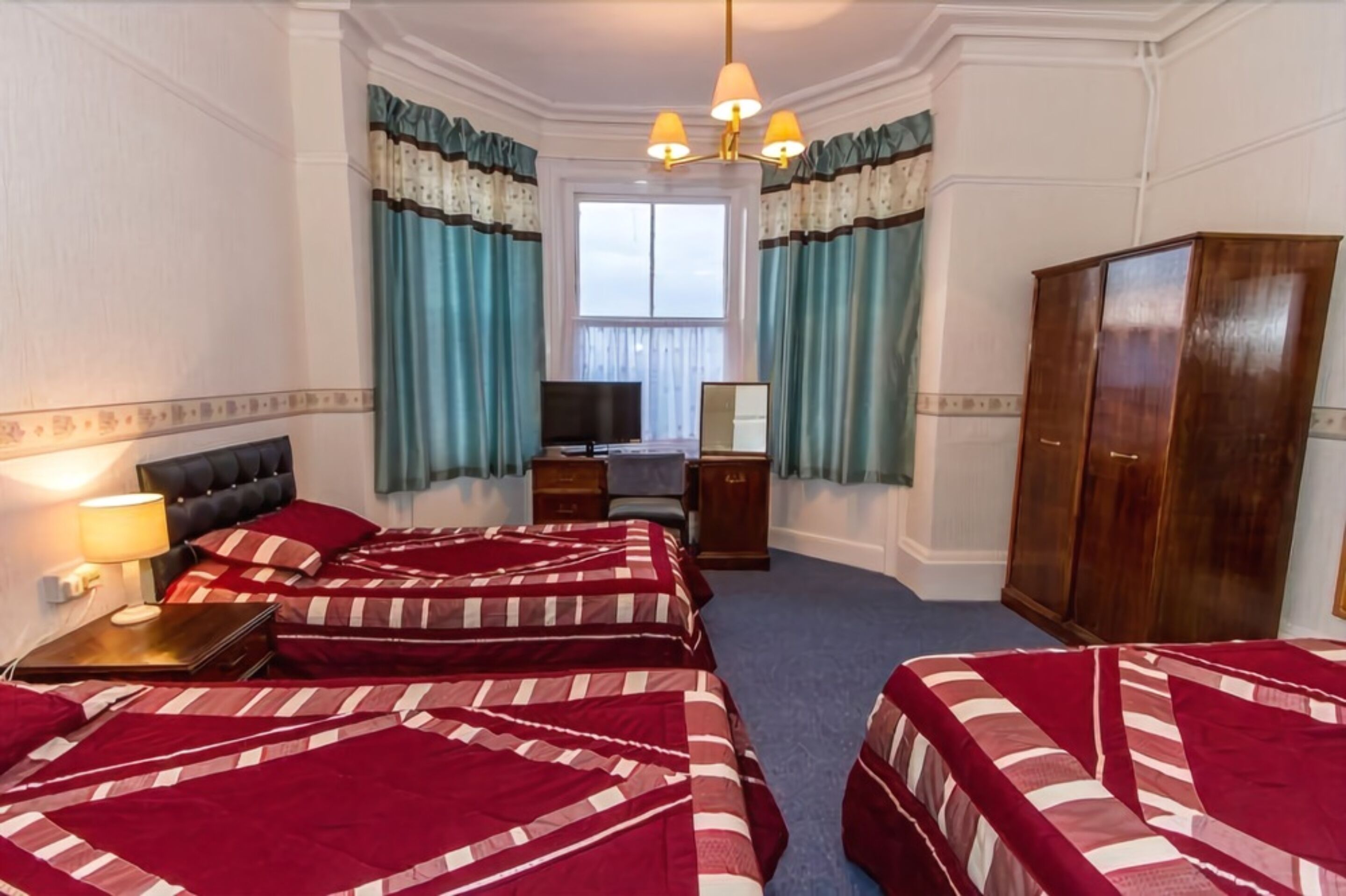 A hotel room with three beds, a desk, a wardrobe, and a television.