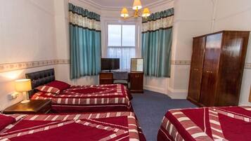 A hotel room with three beds, a desk, a wardrobe, and a television.