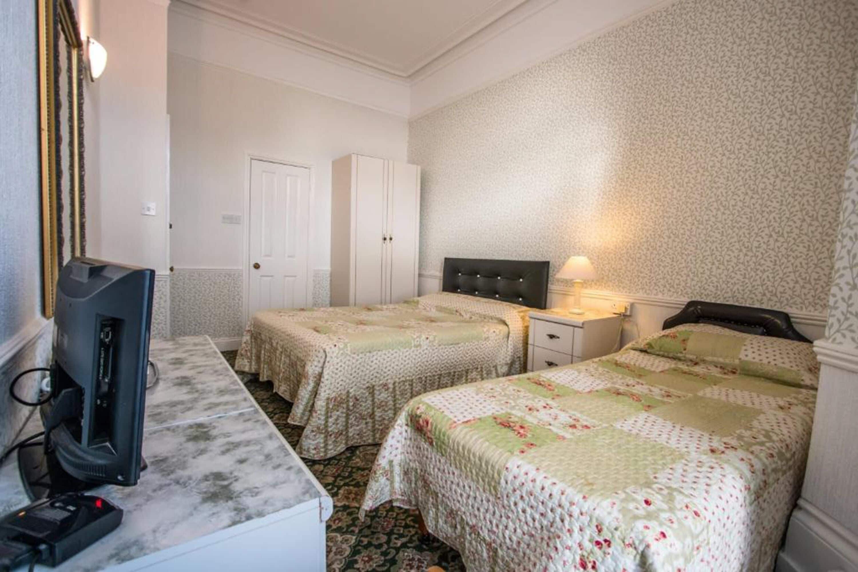A hotel room with two beds, a desk with a computer, a lamp, and a wardrobe.