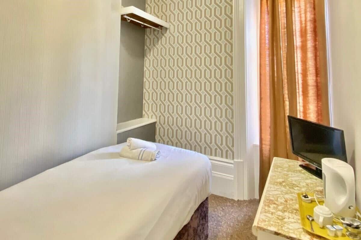 A hotel room with a bed, a desk with a computer, a chair, and a window with curtains.