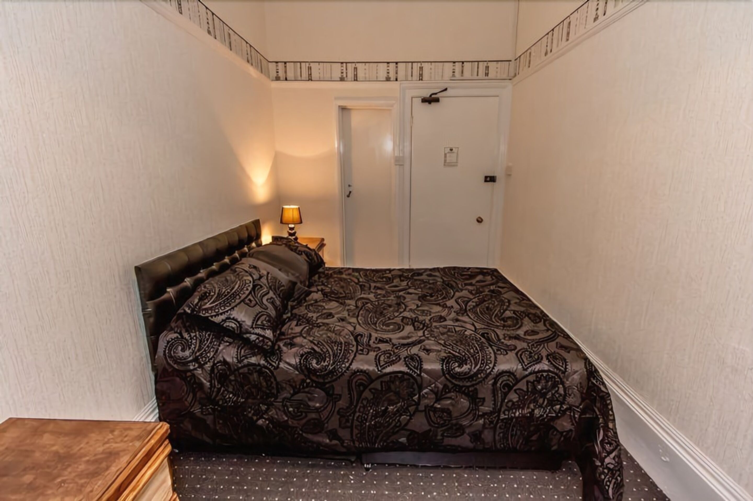 Ein Schlafzimmer mit einem großen Bett, einem Nachttisch, einer Lampe und einer Tür.