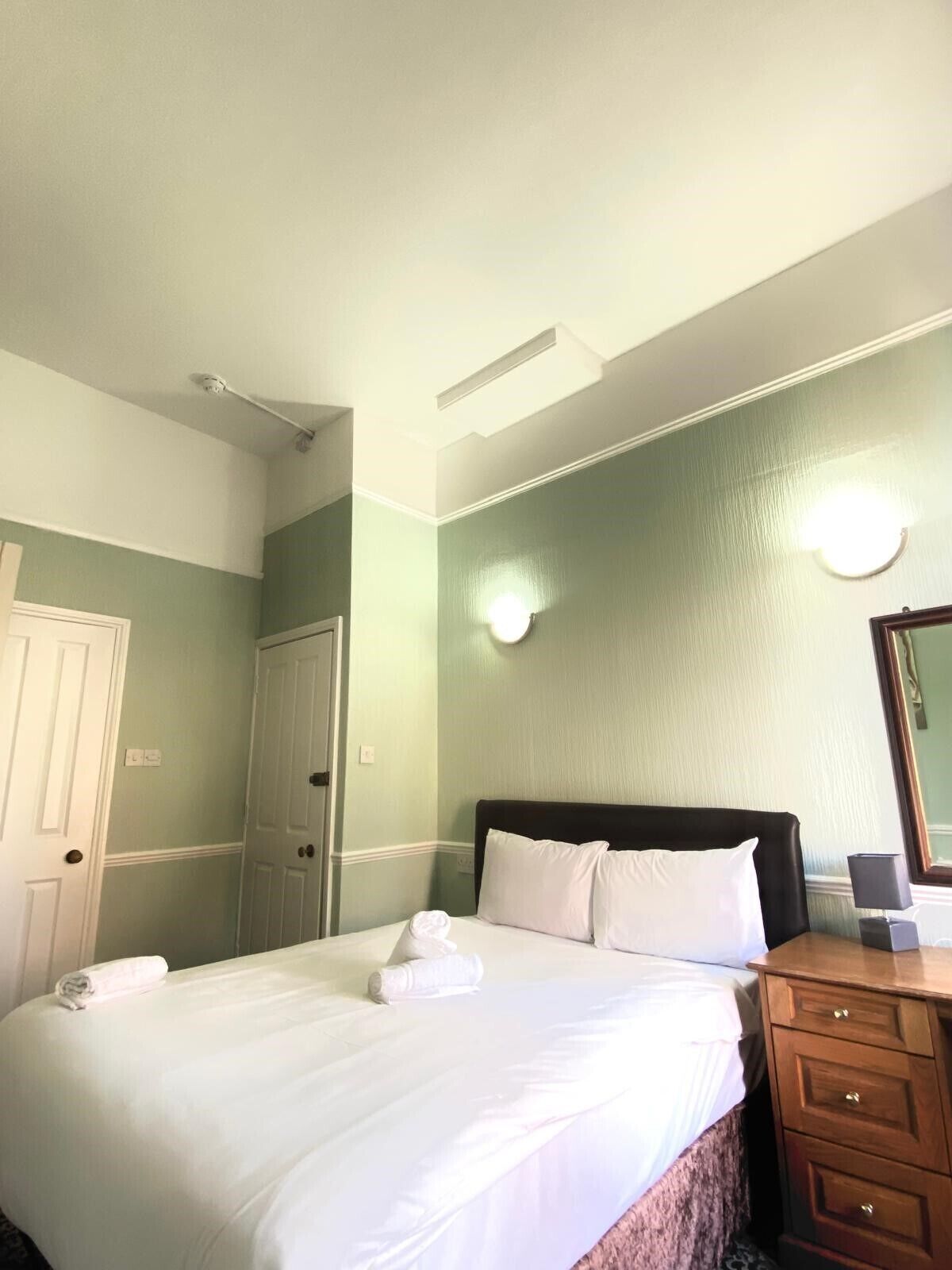 Una habitación de hotel con una cama, un tocador, un espejo y una puerta.