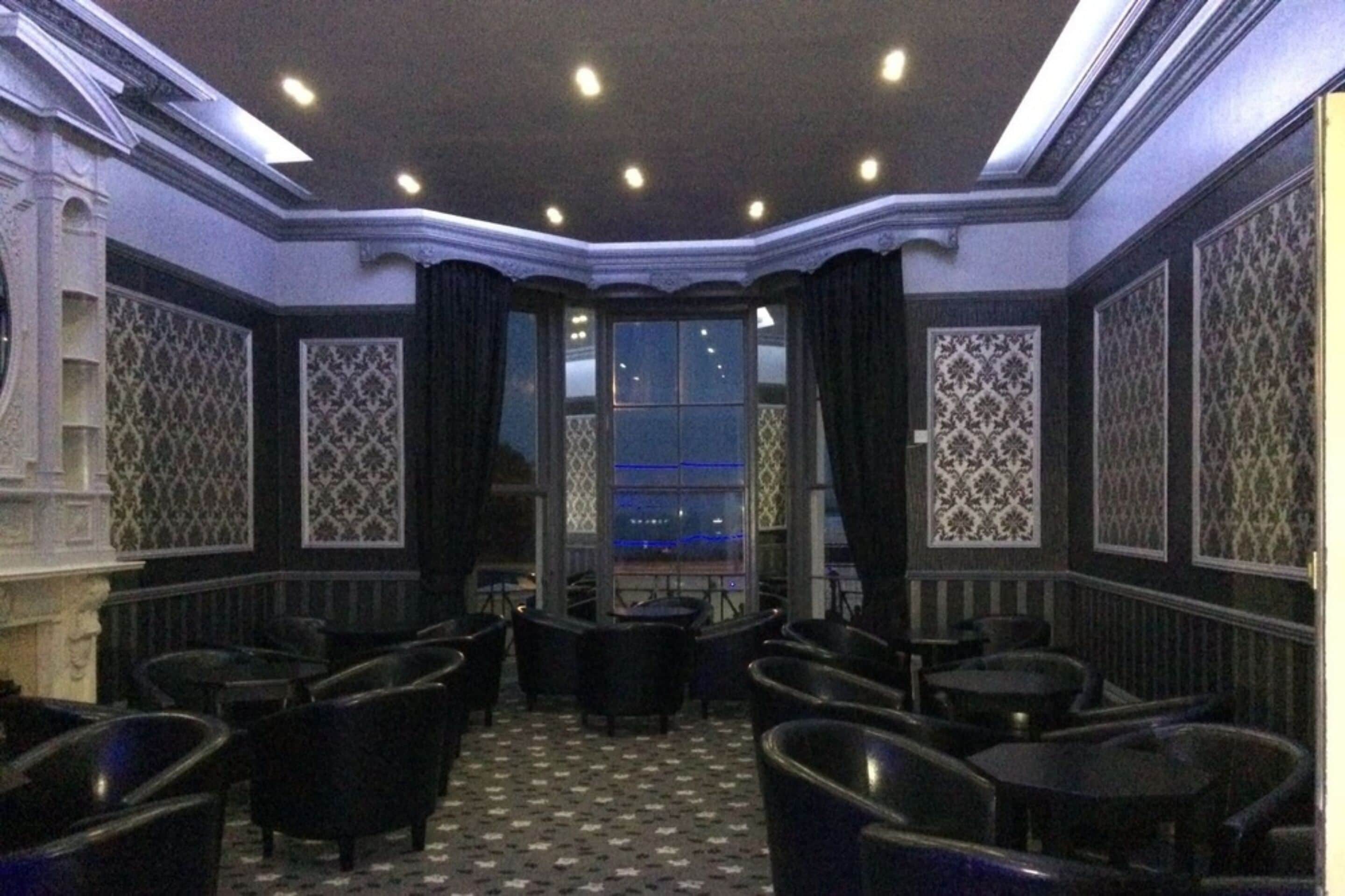 A room with a checkered floor, black upholstered chairs, and patterned walls.