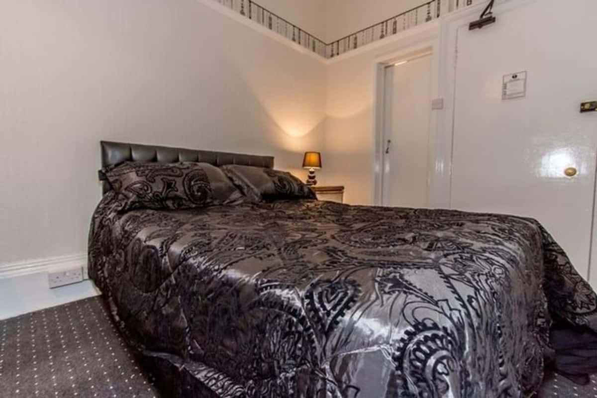 A neatly made bed with a patterned bedspread, a bedside lamp, and a door with a lock.