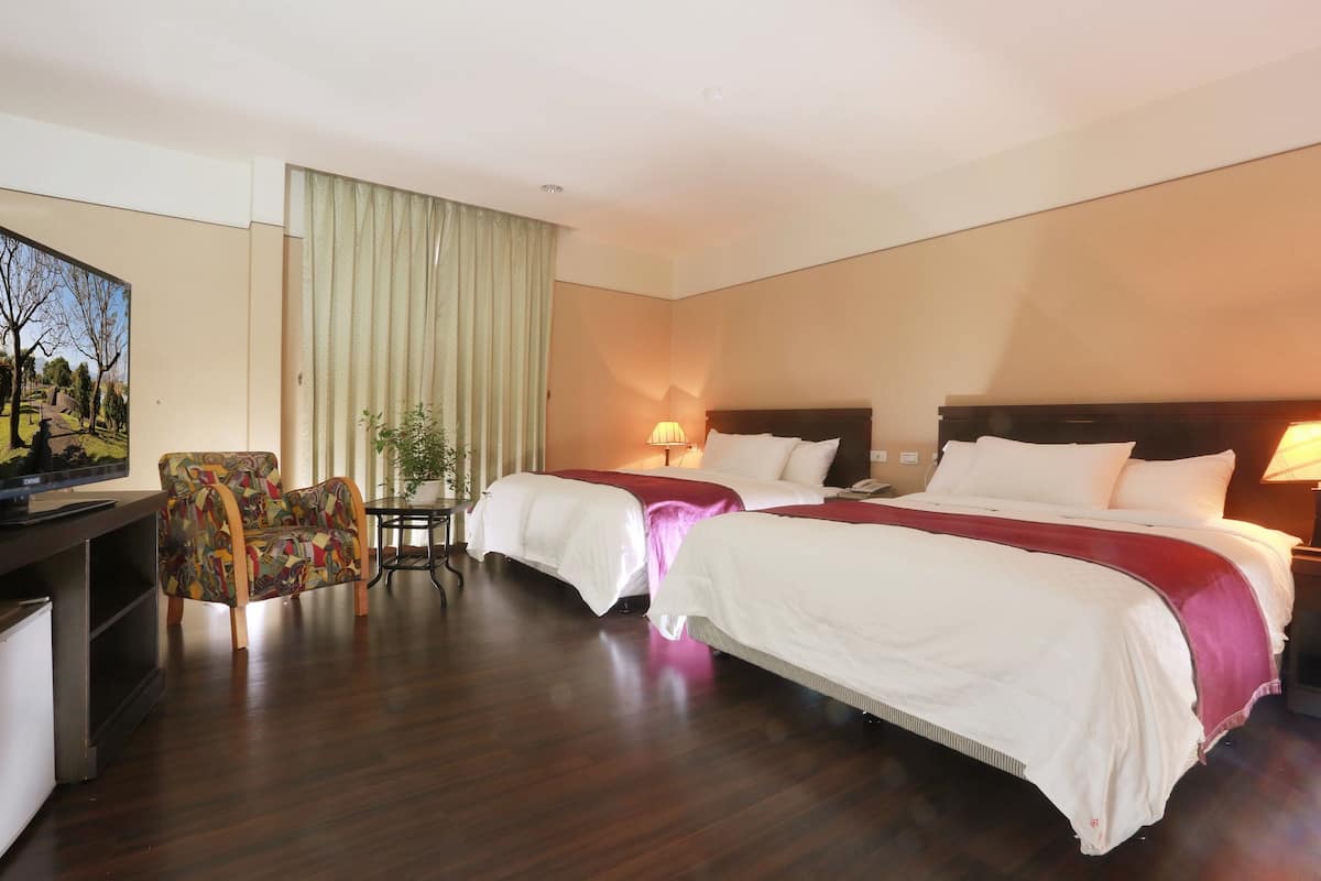 A hotel room with two beds, a desk with a computer, a chair, and a TV.