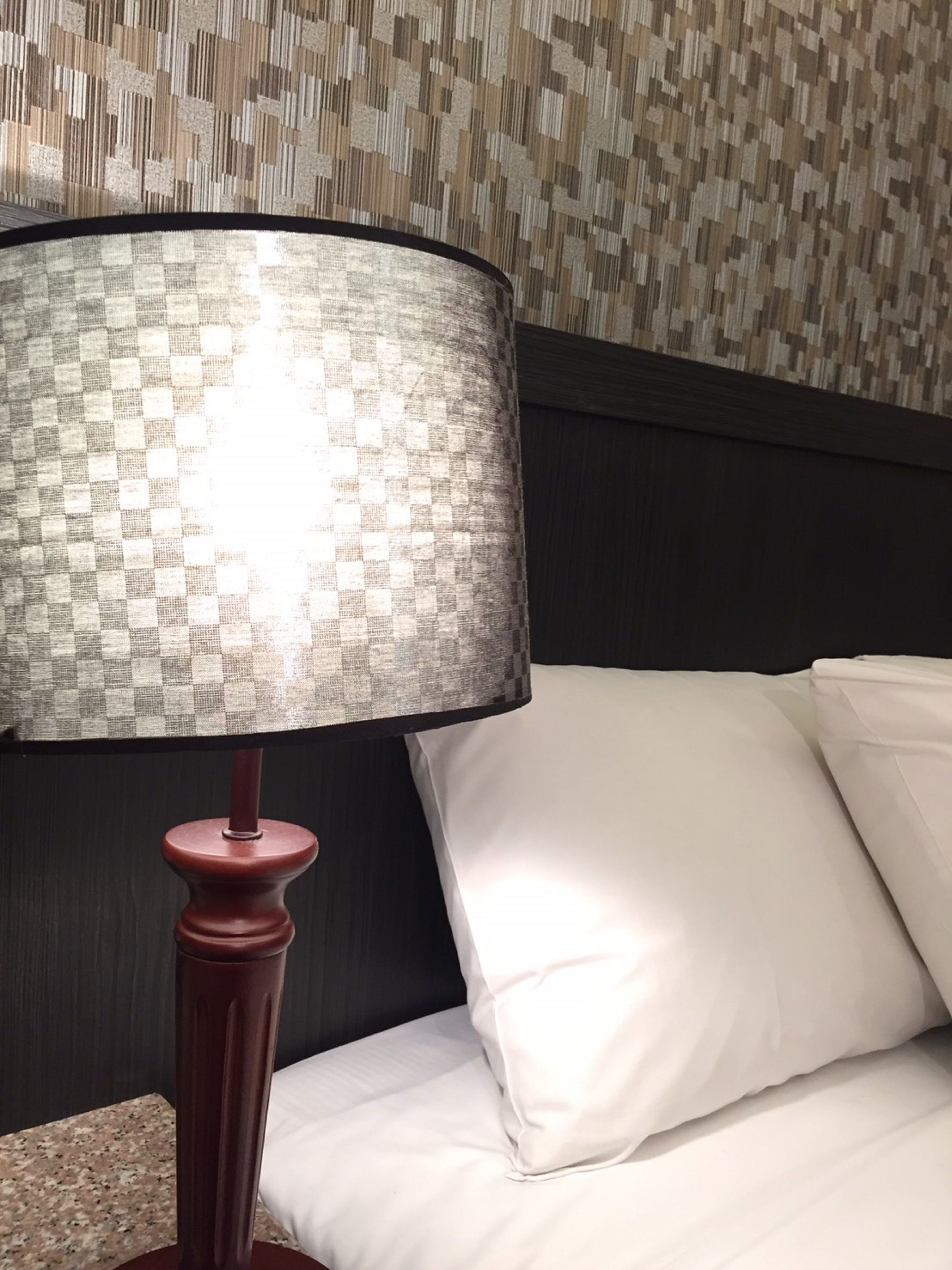 A bed with white bedding and a lamp with a checkered lampshade.