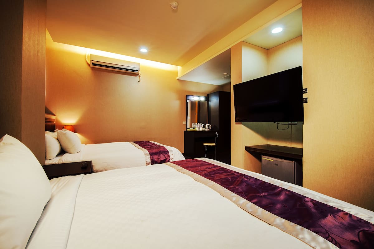 A hotel room with two beds, a flat-screen TV, a desk, and a mirror.